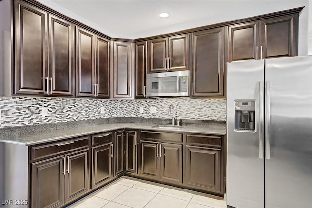 kitchen with dark brown cabinets, dark countertops, a sink, stainless steel appliances, and light tile patterned floors