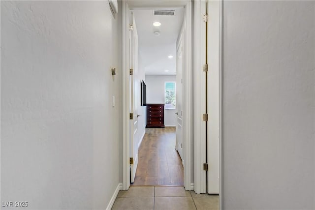 hallway with light tile patterned floors, baseboards, and visible vents