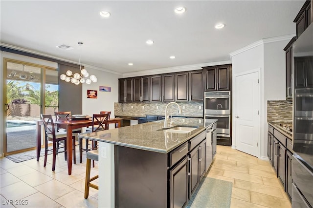 kitchen featuring crown molding, decorative backsplash, a kitchen island with sink, stainless steel double oven, and a sink