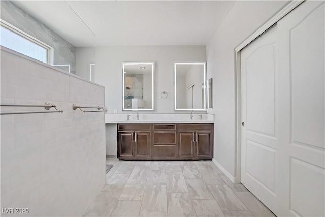 full bath with double vanity, walk in shower, a sink, and marble finish floor