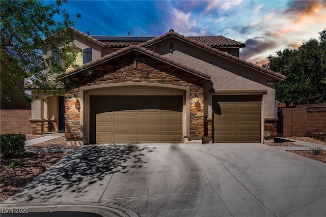 mediterranean / spanish-style home featuring a garage, roof mounted solar panels, stone siding, and concrete driveway