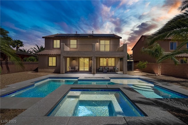 back of property with a balcony, a patio, a fenced backyard, an in ground hot tub, and solar panels