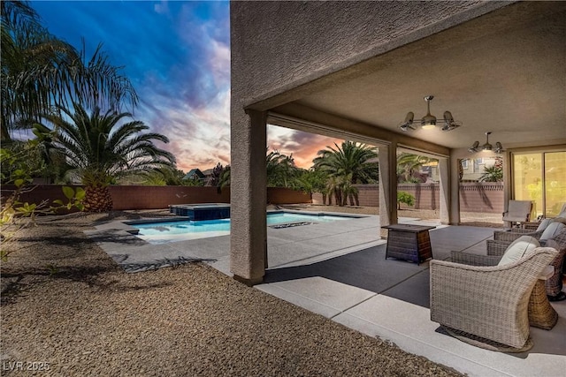 pool at dusk featuring a fenced backyard, a patio area, and a pool with connected hot tub