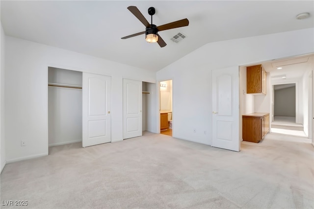unfurnished bedroom with lofted ceiling, light carpet, multiple closets, and visible vents