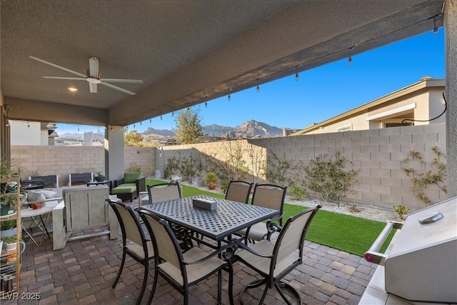 view of patio featuring outdoor dining space, a fenced backyard, a mountain view, and ceiling fan