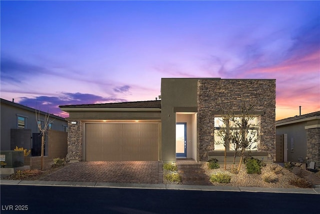 contemporary house featuring an attached garage, stone siding, decorative driveway, and stucco siding