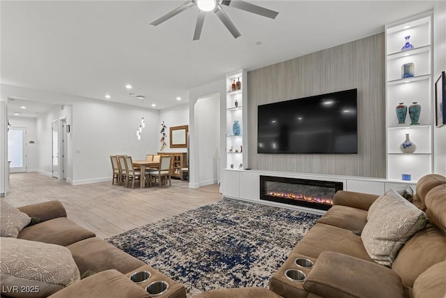 living room featuring a glass covered fireplace, a ceiling fan, recessed lighting, baseboards, and built in shelves