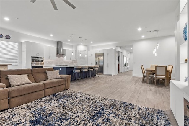 living room with ceiling fan, recessed lighting, baseboards, and light wood finished floors