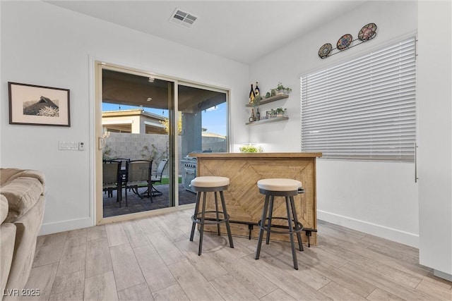 dining space with light wood-style flooring, a dry bar, baseboards, and visible vents