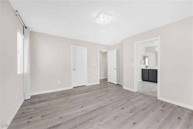 unfurnished bedroom featuring ensuite bath, baseboards, and light wood-style floors