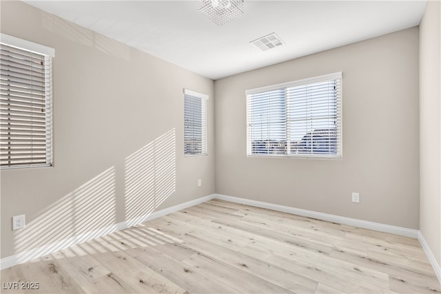 empty room featuring light wood finished floors, baseboards, visible vents, and a healthy amount of sunlight