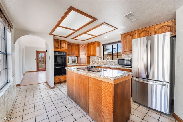 6861 E Washington Ave, Las Vegas, NV 89110 - kitchen with black appliances, light tile patterned floors, arched walkways, a kitchen island, and brown cabinets