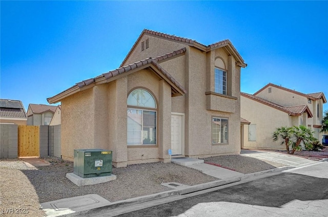 view of front facade with stucco siding, fence, a tile roof, and a gate