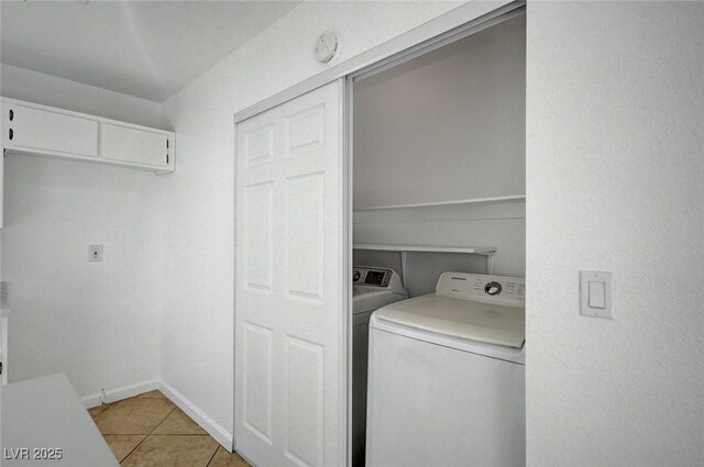 clothes washing area featuring light tile patterned floors, washing machine and clothes dryer, laundry area, and baseboards