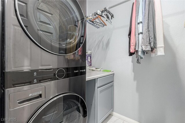 laundry room with stacked washer and clothes dryer, cabinet space, marble finish floor, and baseboards