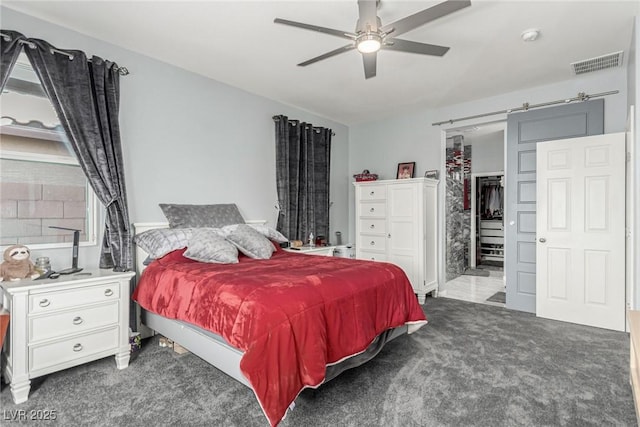 carpeted bedroom with a barn door, a closet, ceiling fan, visible vents, and a spacious closet