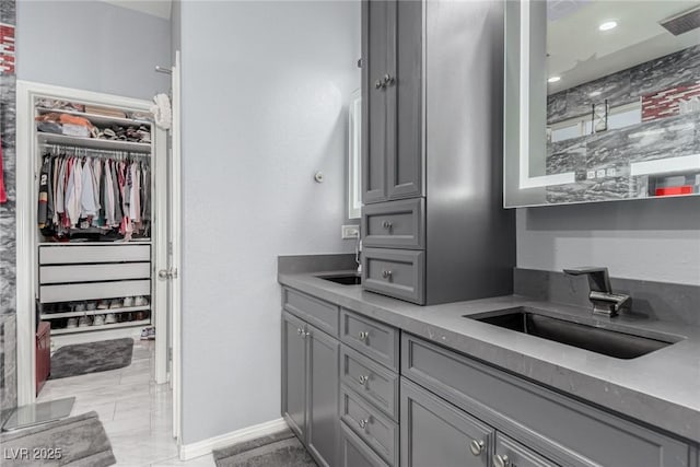 full bath featuring a sink, double vanity, visible vents, baseboards, and a walk in closet