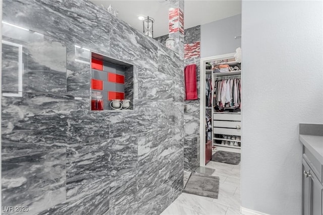 bathroom with a spacious closet, vanity, and marble finish floor