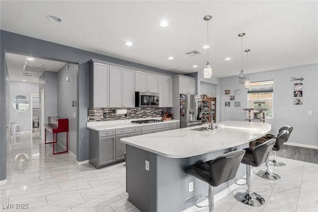 kitchen with a sink, visible vents, gray cabinetry, stainless steel appliances, and a kitchen bar