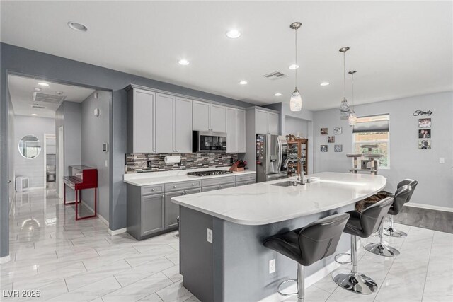 7386 Campbell Ranch Ave, Las Vegas, NV 89179 - kitchen with appliances with stainless steel finishes, gray cabinetry, a sink, a kitchen breakfast bar, and a kitchen island with sink