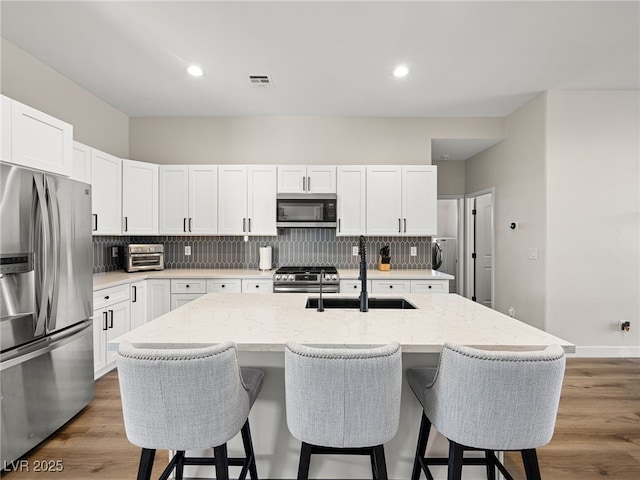 kitchen with visible vents, a breakfast bar, a sink, backsplash, and stainless steel appliances