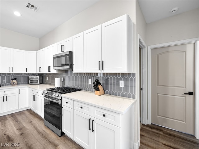 kitchen featuring appliances with stainless steel finishes, tasteful backsplash, wood finished floors, and a toaster