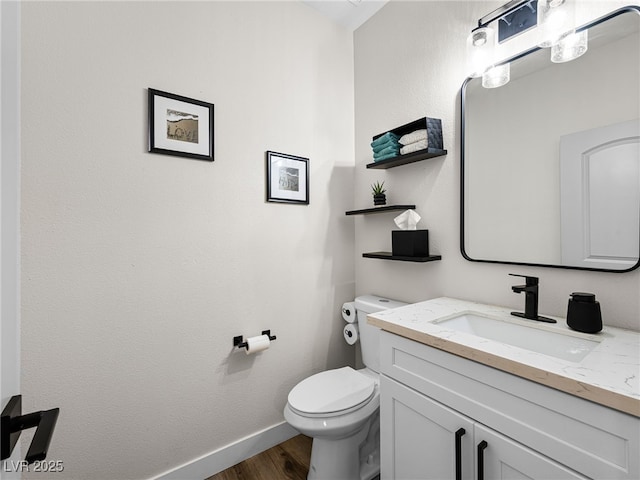 half bath with baseboards, wood finished floors, toilet, and vanity