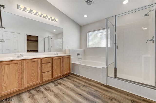 full bathroom featuring a shower stall, lofted ceiling, a garden tub, wood finished floors, and double vanity
