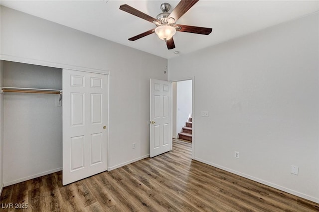 unfurnished bedroom with wood finished floors, a closet, baseboards, and a ceiling fan