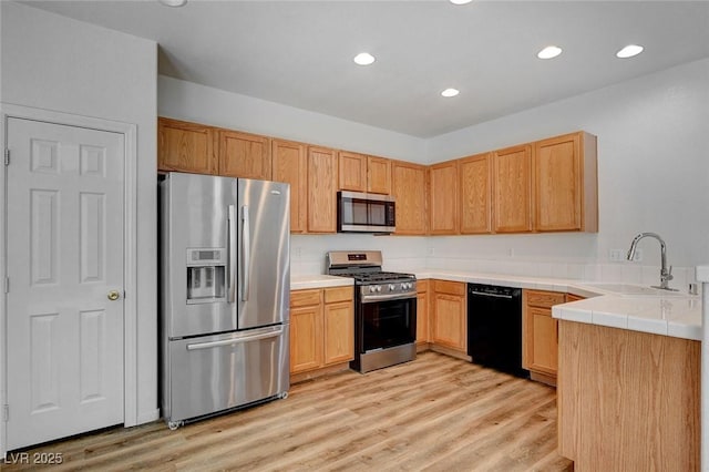 kitchen with stainless steel appliances, a sink, recessed lighting, light wood-style floors, and tile countertops