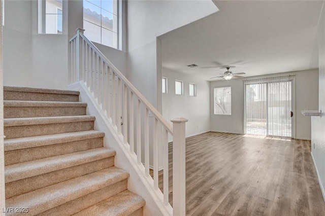 stairway with plenty of natural light, wood finished floors, a ceiling fan, and baseboards