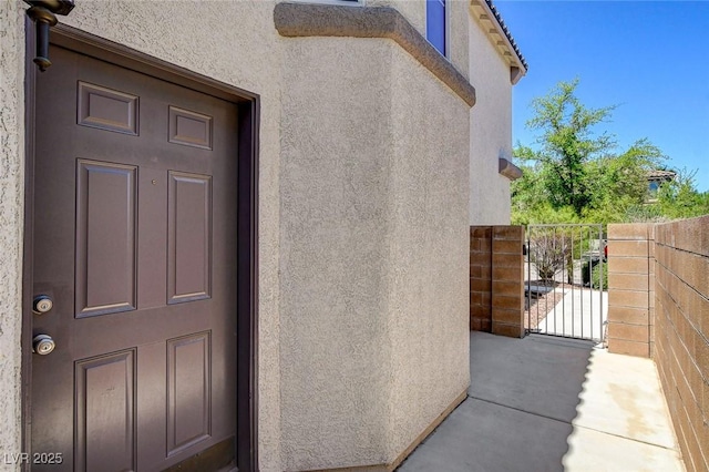property entrance with stucco siding, a gate, and fence