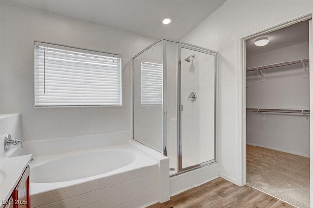 bathroom with a stall shower, a spacious closet, a bath, and wood finished floors