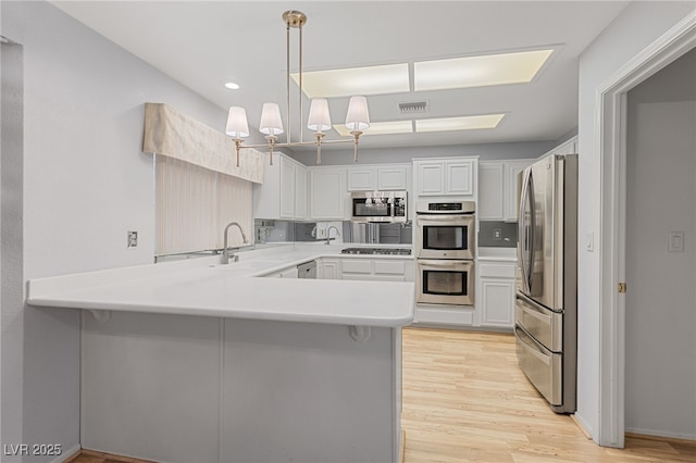 kitchen with a peninsula, a sink, stainless steel appliances, visible vents, and light countertops