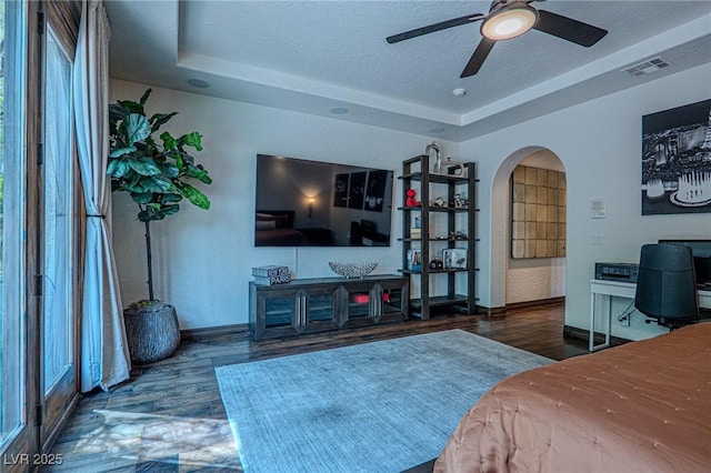11814 Canons Brook Dr, Las Vegas, NV 89141 - bedroom featuring visible vents, baseboards, arched walkways, a tray ceiling, and wood finished floors