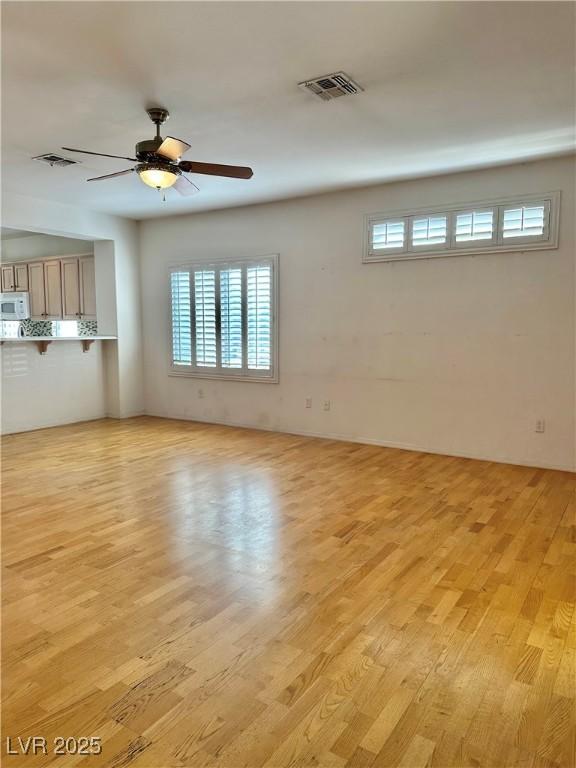spare room with visible vents, ceiling fan, light wood-type flooring, and a healthy amount of sunlight