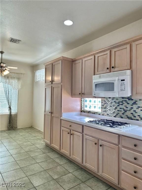 kitchen with decorative backsplash, light brown cabinets, light tile patterned floors, white appliances, and light countertops