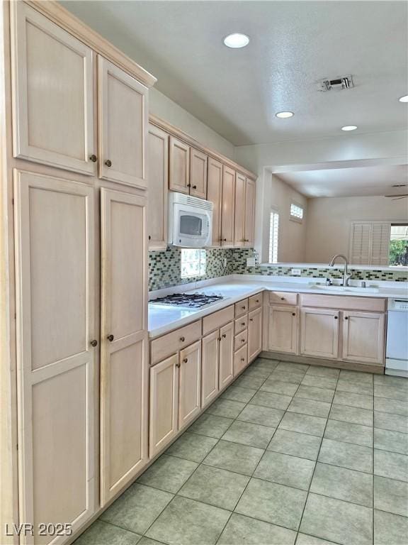 kitchen featuring a sink, visible vents, light countertops, white appliances, and backsplash