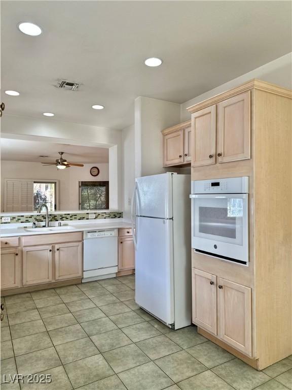 kitchen featuring white appliances, light brown cabinets, a sink, visible vents, and a ceiling fan