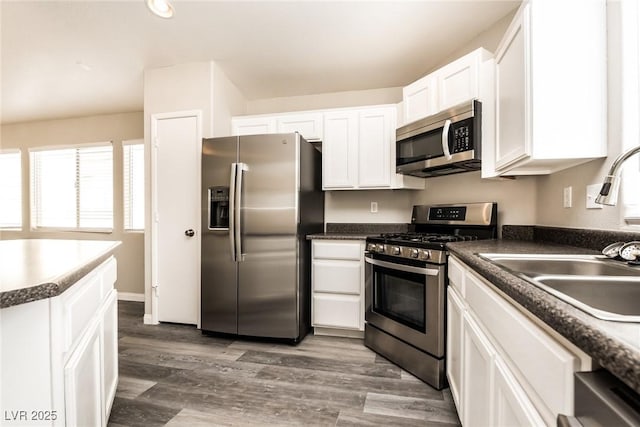 3434 Denali Preserve St, Las Vegas, NV 89122 - kitchen featuring dark countertops, white cabinets, stainless steel appliances, a sink, and wood finished floors