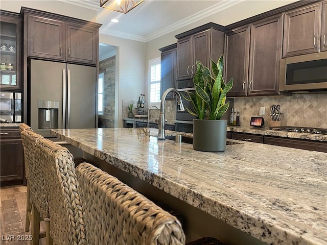kitchen featuring ornamental molding, a breakfast bar area, light stone counters, and stainless steel appliances