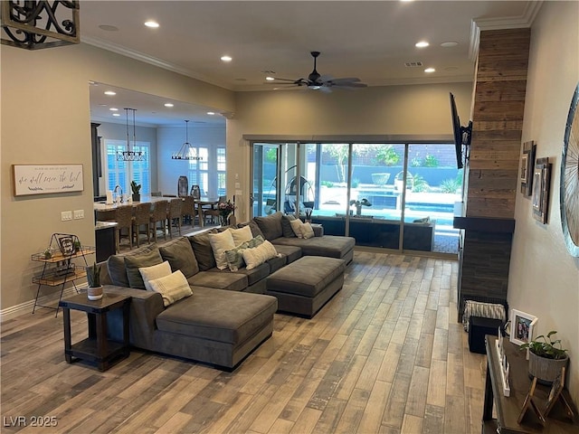 living room featuring recessed lighting, light wood finished floors, ceiling fan with notable chandelier, and crown molding