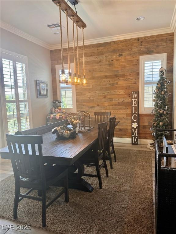dining space featuring wooden walls, visible vents, baseboards, and crown molding