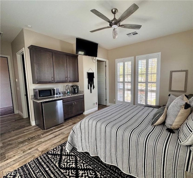 bedroom with visible vents, baseboards, a sink, light wood-type flooring, and a ceiling fan