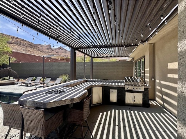 view of patio with a mountain view, an outdoor fire pit, grilling area, a fenced backyard, and an outdoor kitchen