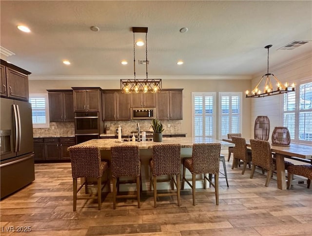 kitchen with dark brown cabinetry, visible vents, appliances with stainless steel finishes, a sink, and a notable chandelier