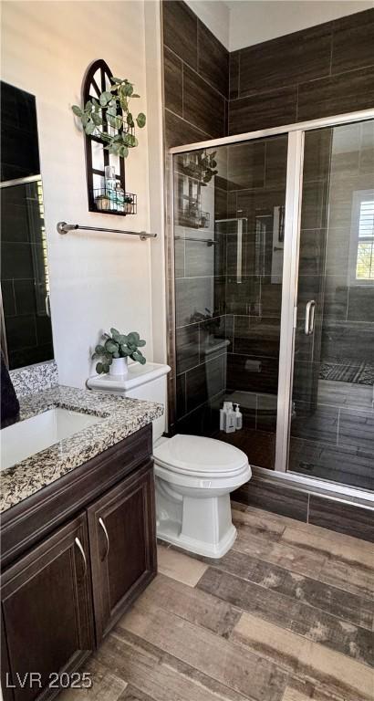 bathroom featuring a shower stall, wood finished floors, vanity, and toilet