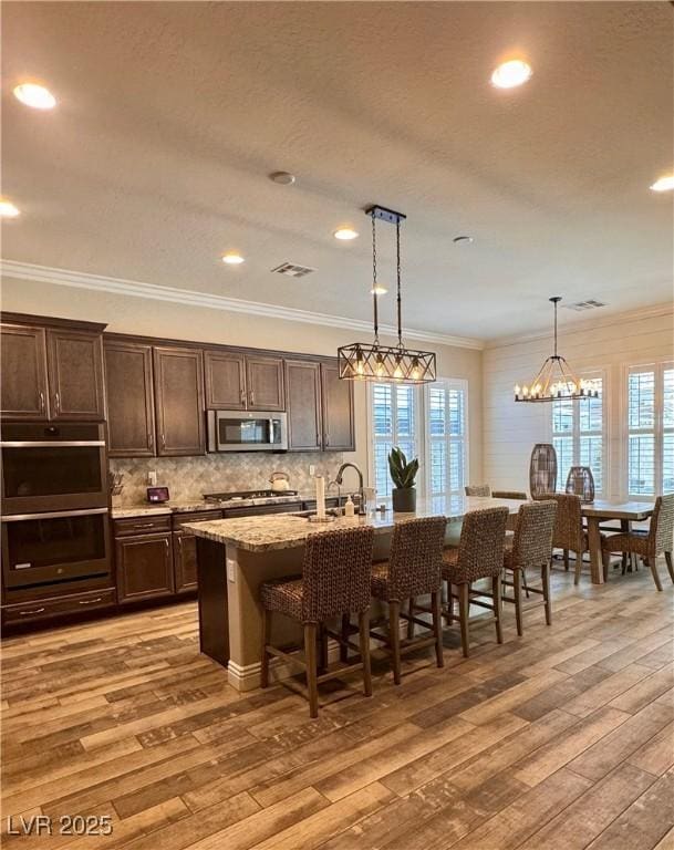 kitchen featuring appliances with stainless steel finishes, dark brown cabinets, light wood finished floors, decorative backsplash, and a breakfast bar area