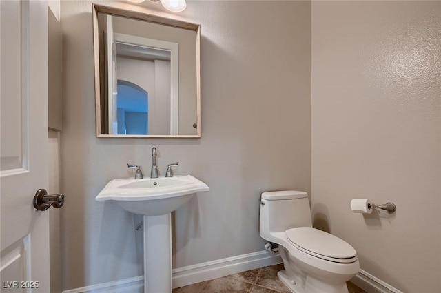 half bath featuring tile patterned flooring, baseboards, a sink, and toilet