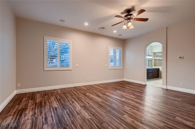 unfurnished room with baseboards, a ceiling fan, visible vents, dark wood finished floors, and arched walkways